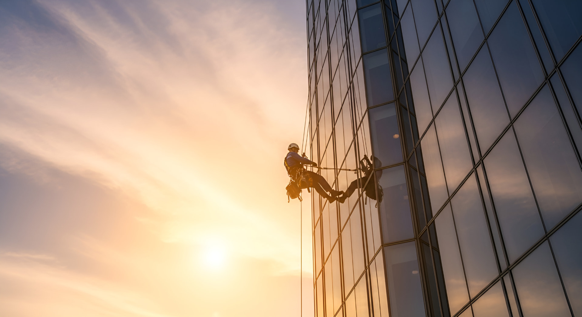 Travailleur en descente sur corde nettoyant la façade vitrée d'une tour au coucher du soleil