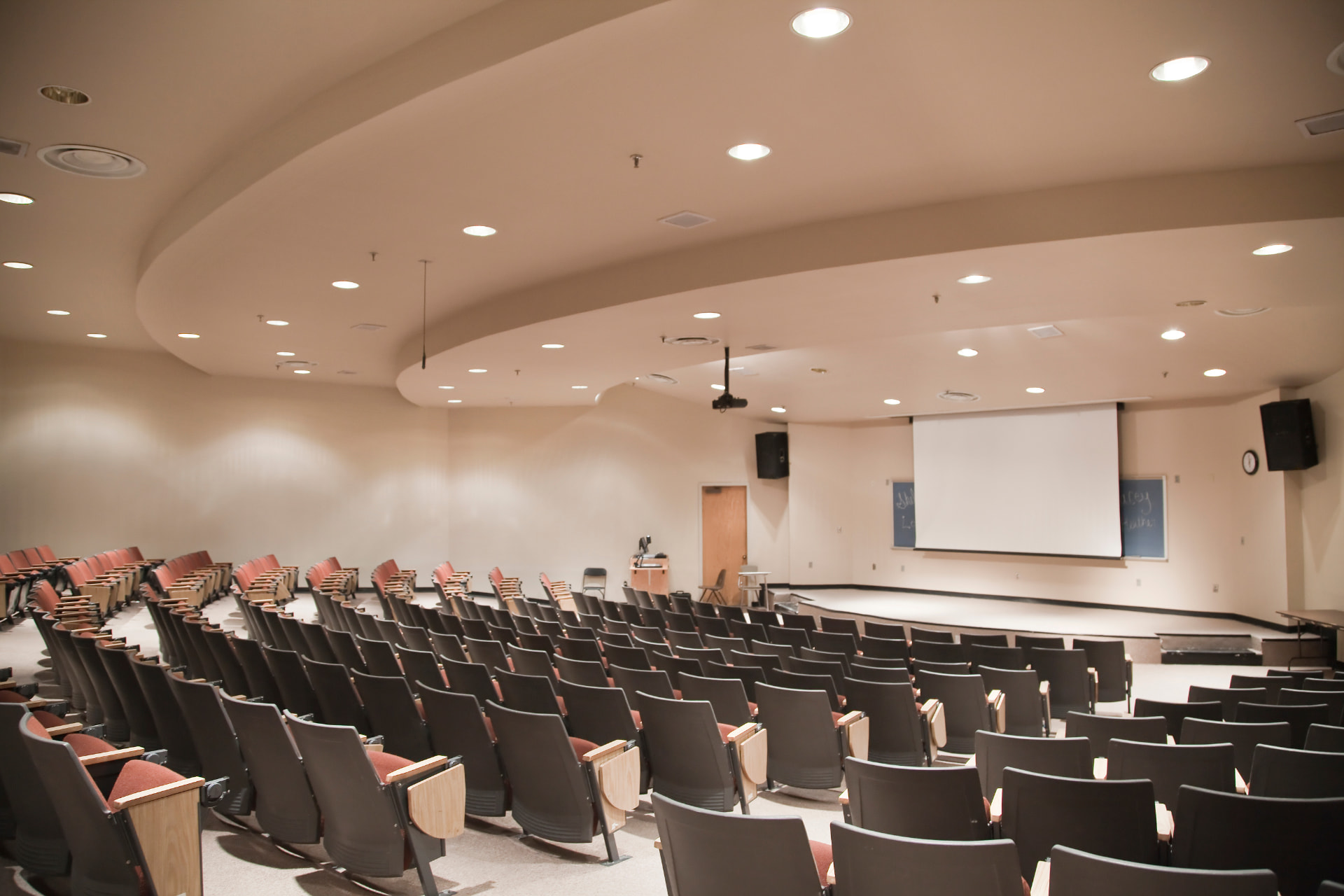 Amphithéâtre scolaire vide, rangées de fauteuils et écran de projection
