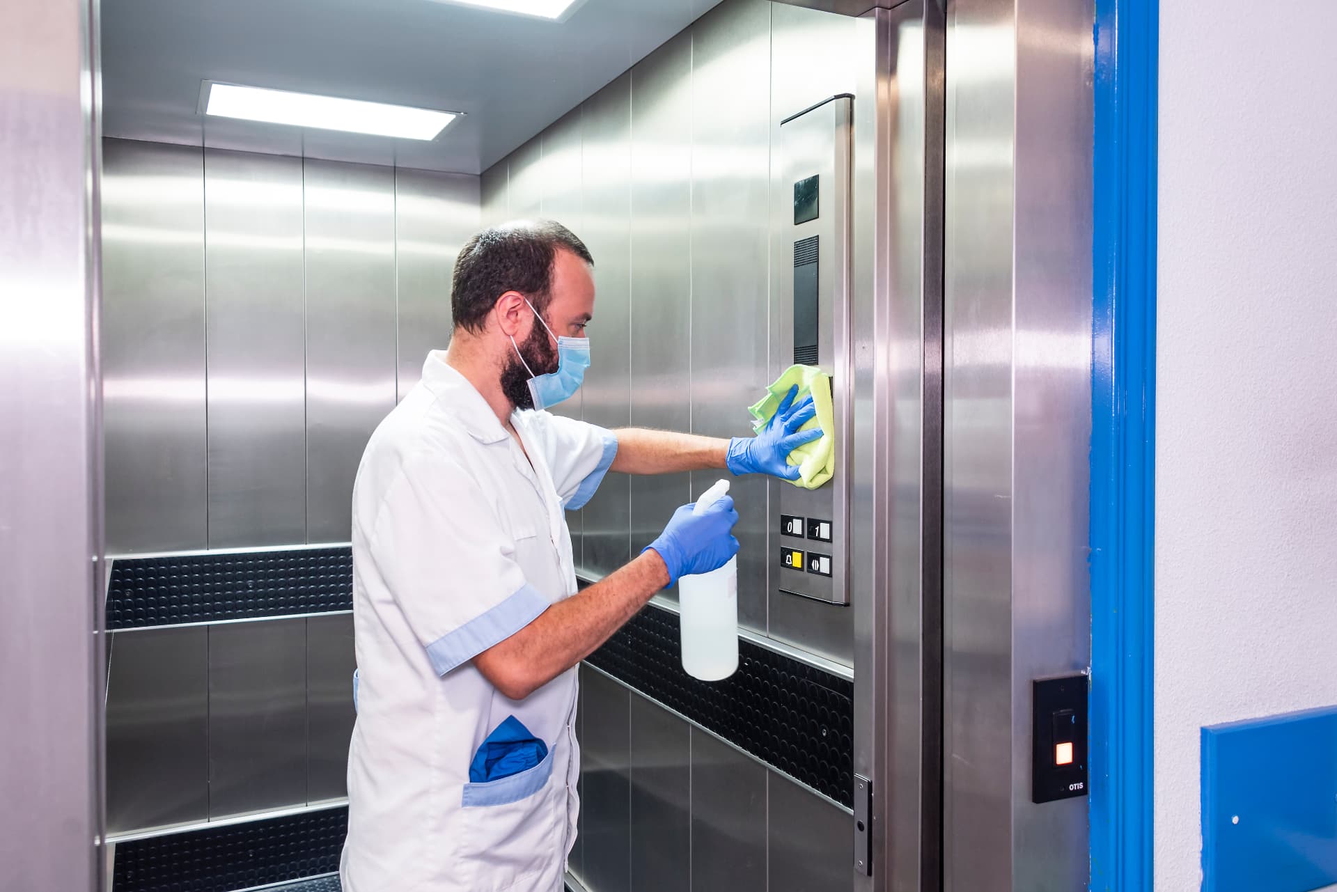 Préposé masqué désinfectant le panneau de commande d'un ascenseur en acier inoxydable